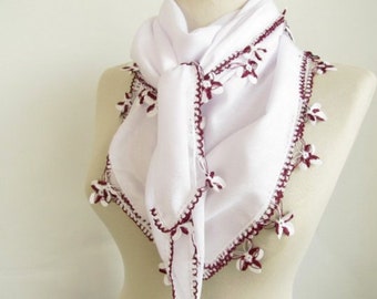 Pode incluir: Cachecol triangular branco com uma borda de crochê bordô e pequenos detalhes de flores.