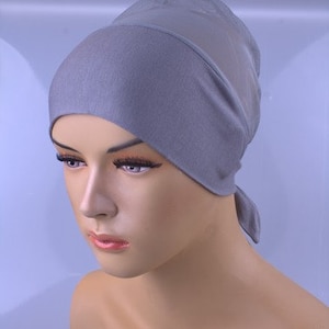 May include: A grey, soft, stretchy fabric head covering with a tie at the back. The head covering is designed to be worn under a hijab.