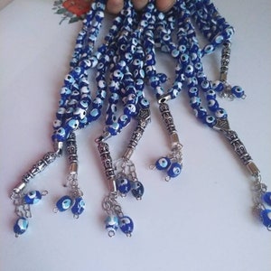 Peut inclure: Un ensemble de cinq chapelets bleus et blancs avec des breloques argent&eacute;es. Chaque perle pr&eacute;sente un motif d'&oelig;il bleu mal&eacute;fique. Les breloques sont d&eacute;cor&eacute;es de motifs argent&eacute;s complexes.