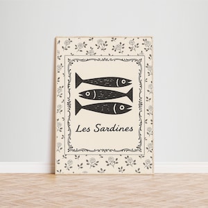 May include: A rectangular wooden sign featuring three black fish illustrations above the text "Les Sardines". The sign has a cream-colored background with a decorative black border and floral accents.