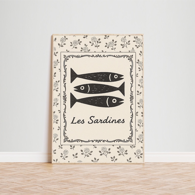 May include: A rectangular wooden sign featuring three black fish illustrations above the text "Les Sardines". The sign has a cream-colored background with a decorative black border and floral accents.