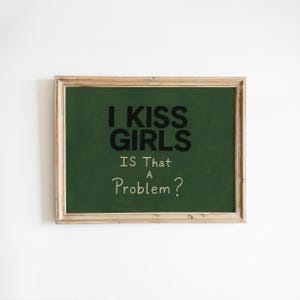 May include: A framed chalkboard with the text "I KISS GIRLS IS That A Problem?" in black and white. The chalkboard has a green background and a light brown wooden frame. The text is centered on the board.