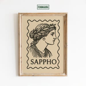 May include: Framed art print featuring a black and white illustration of Sappho, a Greek poet, in profile. The artwork is set against a beige background within a decorative stamp-like border. The word "SAPPHO" is printed below the image.
