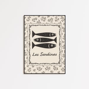 May include: Black framed art print featuring three stylized black fish above the words "Les Sardines". The artwork has a beige background with a decorative border and a floral pattern.