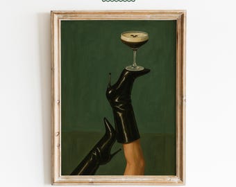 Pode incluir: Impressão artística emoldurada com um copo de cocktail equilibrado numa bota preta de salto alto. O fundo é verde escuro e a moldura é de madeira clara. O texto "FEMMAURA" está no canto superior.