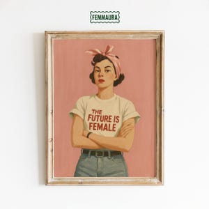Può includere: Stampa artistica incorniciata con un'illustrazione vintage di una donna con un foulard rosa e una maglietta bianca. La maglietta ha il testo rosso "THE FUTURE IS FEMALE". Lo sfondo è di colore rosa.