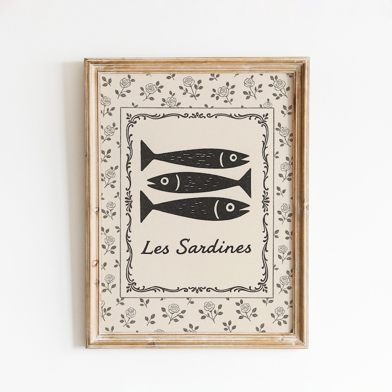 May include: Framed art print featuring three stylized black fish on a beige background, with the text "Les Sardines" below. The print is surrounded by a decorative border and a floral pattern, all within a wooden frame.