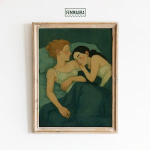 May include: Framed art print featuring two women in a bed, one with auburn hair and the other with dark hair, both asleep. The artwork is in shades of green and cream, with the text "FEMMAURA" at the top.