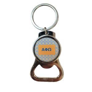 Könnte beinhalten: Ein silberner Flaschenöffner-Schlüsselanhänger mit einem runden, orangefarbenen und blauen Muster, das die griechischen Buchstaben "ΑΦΩ" zeigt.