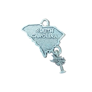 May include: Silver charm in the shape of the state of South Carolina with the words "South Carolina" inscribed on the charm. A small silver palm tree charm is attached to the bottom of the state charm.