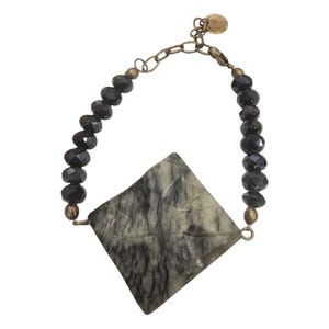 Puede incluir: Un brazalete de cuentas negras con un gran colgante cuadrado de piedra verde y negra.