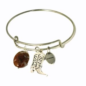 May include: A silver expandable bangle bracelet with three charms: a brown stone, a silver boot charm, and a silver charm with the word "Grandma" engraved on it.