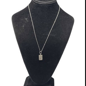 May include: A silver chain necklace with a small rectangular pendant. The pendant has a textured design.