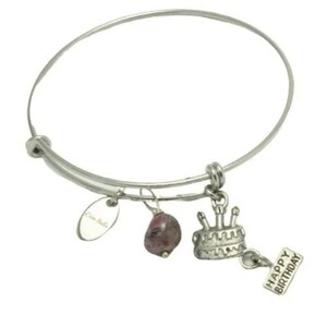 May include: Silver expandable bracelet with a charm of a birthday cake with candles, a pink stone, and a tag that says "Happy Birthday".