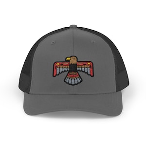 May include: A gray trucker hat with a black mesh back and a colorful embroidered eagle emblem. The eagle design features red, yellow, and blue accents. The hat is a classic accessory.