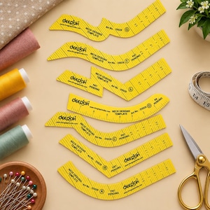 Pode incluir: Um conjunto de sete moldes amarelos de plástico para designs de decotes, rotulados de A a G, com marcações pretas, medidas e a marca Deepak. Estas ferramentas de costura estão dispostas ao lado de carretéis de linha, alfinetes e tesouras.
