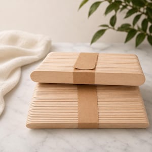 Könnte beinhalten: Zwei Stapel aus hellen Holz-Bastelstäbchen, wobei jedes Bündel mit einem schlichten braunen Papierstreifen zusammengehalten wird. Die Stäbchen sind flach, rechteckig und haben abgerundete Enden, die in ordentlichen, horizontalen Schichten liegen.