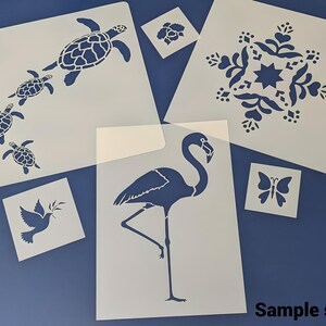 Pode incluir: Um conjunto de seis stencils com v&aacute;rios desenhos, incluindo um flamingo, uma borboleta, uma pomba, um floco de neve e um grupo de tartarugas marinhas. Os stencils s&atilde;o feitos de pl&aacute;stico branco e est&atilde;o dispostos sobre uma superf&iacute;cie azul. O texto "Sample stencils" &eacute; vis&iacute;vel na parte inferior da imagem.