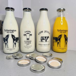 May include: Four glass milk bottles with black lids and silver caps. Three bottles contain white liquid, and one contains yellow liquid. The bottles have labels with cow illustrations and text, including "Tytherington Milk Station" and "Cow Juice."