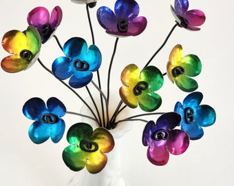 Könnte beinhalten: Ein Strauß bunter Metallblumen in einer weißen Vase. Die Blumen sind aus Metall und haben eine Regenbogen-Oberfläche. Jede Blume hat eine schwarze Metallmitte.