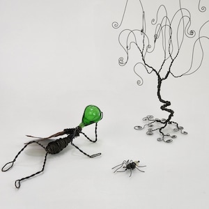 May include: A green glass bottle with a wire body and legs, a black wire spider, and a black wire tree with curly branches.