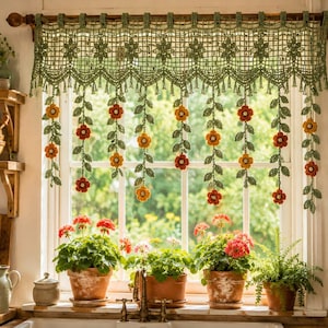 May include: A sage green crocheted window valance featuring a grid pattern with floral motifs and hanging vertical strands of crocheted green leaves and orange and red flowers, suspended from a wooden curtain rod over a kitchen window.