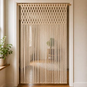 May include: A cream-colored macrame door curtain featuring a top section with a diamond-shaped knotted pattern and a lower section consisting of long, vertical hanging cords suspended from a horizontal wooden rod within a doorway frame.