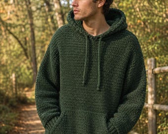 Puede incluir: Una sudadera con capucha de manga larga en color verde bosque oscuro, confeccionada con un patrón de ganchillo visible. La prenda cuenta con capucha con cordones a juego, un bolsillo delantero tipo canguro y puños y dobladillo acanalados.