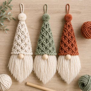 Puede incluir: Tres adornos colgantes de gnomo con sombreros de macram&eacute; en color crema, verde salvia y terracota. Cada gnomo tiene una nariz de cuenta de madera redonda y una larga barba de flecos color crema. Un pomp&oacute;n de hilo a juego corona cada gorro.