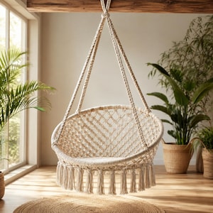 May include: A cream-colored macrame hanging chair featuring a circular seat with a diamond-patterned woven net design. The chair is suspended by thick braided ropes attached to a wooden beam and includes long decorative fringe tassels.