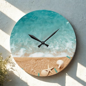 Könnte beinhalten: Runde Wanduhr mit einer Strandszene mit türkisfarbenem Ozean und sandigem Ufer. Das Zifferblatt zeigt einen Seestern, Muscheln und schwarze Zeiger. Die Uhr ist an einer weißen Wand befestigt.