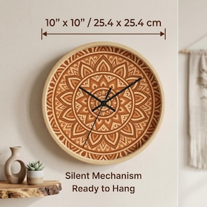 Op de afbeelding: Een ronde houten wandklok, 25,4 cm in diameter, met een gedetailleerd mandala-patroon in bruintinten. De klok heeft zwarte wijzers en een licht houten frame. De tekst op de afbeelding luidt "Silent Mechanism Ready to Hang."