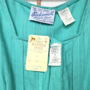 Puede incluir: Un vestido turquesa sin mangas con una etiqueta blanca que dice "Tom's Western Store" y una etiqueta blanca que dice "Tru-West Rockmount Ranch Wear Custom Fitted". El vestido tiene una etiqueta de talla que dice "Talla 12" y una etiqueta de precio que dice "58,95 &euro;".