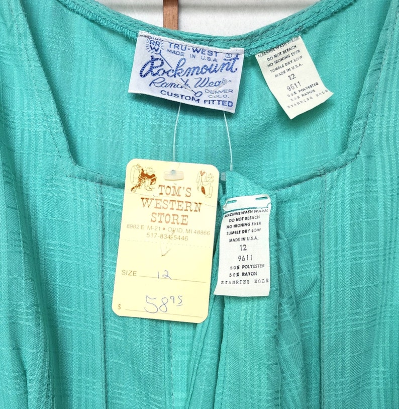 Puede incluir: Un vestido turquesa sin mangas con una etiqueta blanca que dice "Tom's Western Store" y una etiqueta blanca que dice "Tru-West Rockmount Ranch Wear Custom Fitted". El vestido tiene una etiqueta de talla que dice "Talla 12" y una etiqueta de precio que dice "58,95 &euro;".
