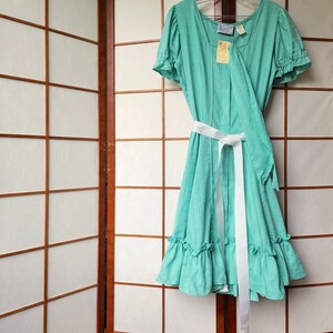 Puede incluir: Un vestido verde menta con rayas blancas y una faja blanca. El vestido tiene un dobladillo con volantes y mangas cortas abullonadas.