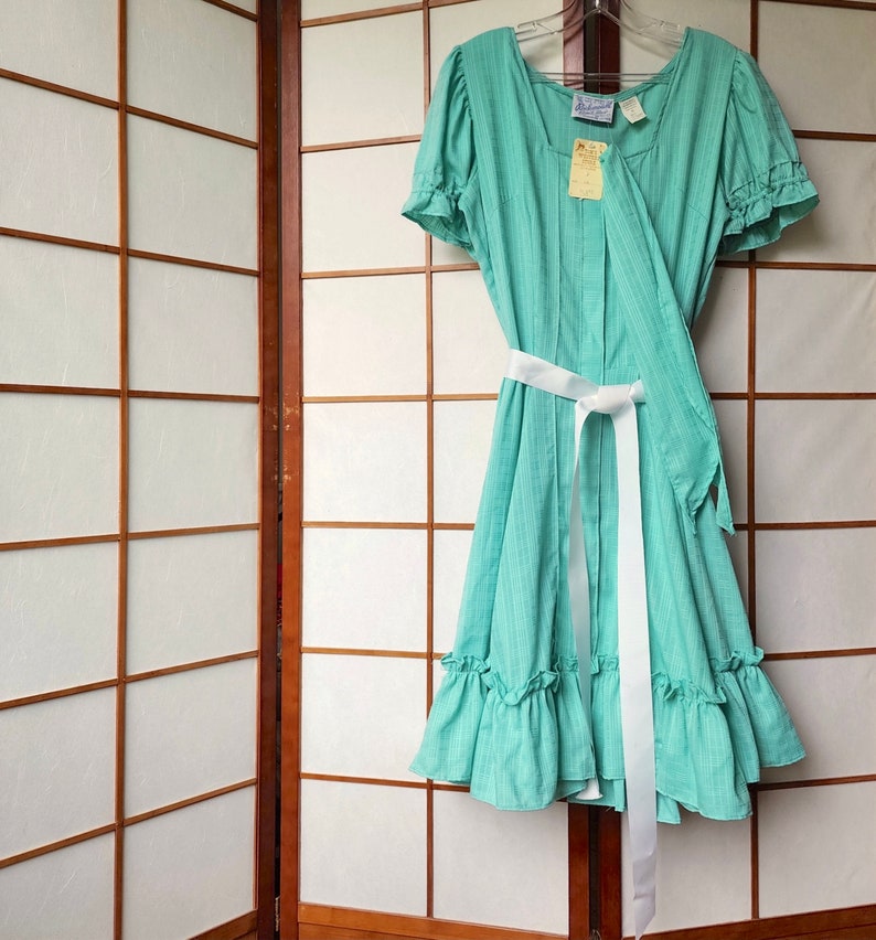 Puede incluir: Un vestido verde menta con rayas blancas y una faja blanca. El vestido tiene un dobladillo con volantes y mangas cortas abullonadas.