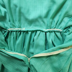 Puede incluir: Primer plano del interior de un vestido verde azulado con una cintura el&aacute;stica blanca y una cremallera.