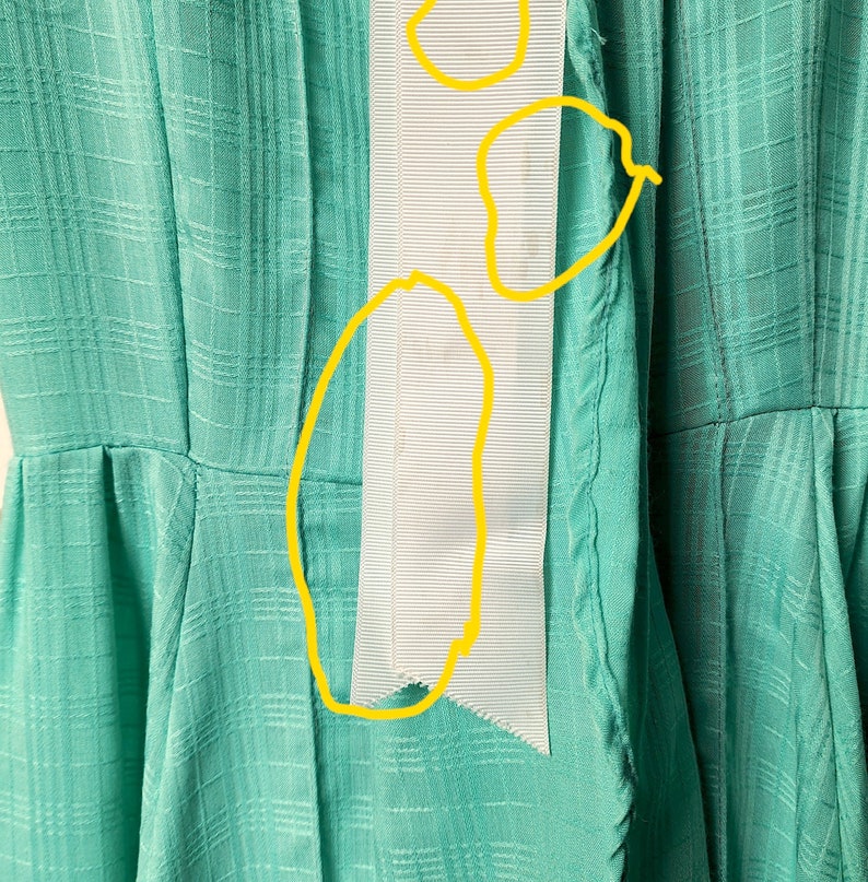 Puede incluir: Un vestido turquesa con un detalle de cinta blanca. La cinta est&aacute; cosida en la parte delantera del vestido y tiene un borde deshilachado.