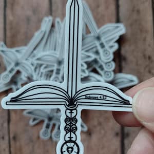 May include: White sticker in the shape of a sword with a cross-shaped hilt and an open book design. The text "Hebrews 4:12" is visible on the sticker. The sticker is held by a person's fingers.