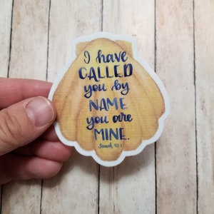 May include: A seashell sticker with the text "I have called you by name you are mine. Isaiah 43:1" in blue lettering.