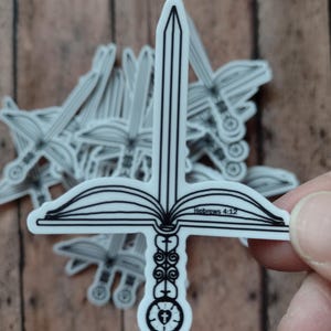 Peut inclure: Autocollant blanc repr&eacute;sentant une &eacute;p&eacute;e combin&eacute;e &agrave; un livre ouvert et une croix. Le texte "H&eacute;breux 4:12" est visible. D'autres autocollants sont en arri&egrave;re-plan.