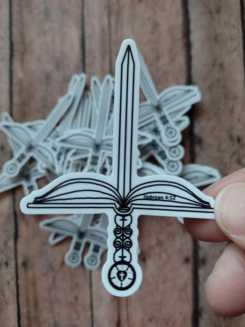Peut inclure: Autocollant blanc repr&eacute;sentant une &eacute;p&eacute;e combin&eacute;e &agrave; un livre ouvert et une croix. Le texte "H&eacute;breux 4:12" est visible. D'autres autocollants sont en arri&egrave;re-plan.