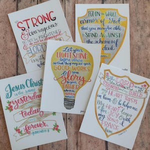 May include: A collection of five white cards with handwritten inspirational quotes and floral accents. The cards feature phrases like "STRONG & courageous" and "Let your LIGHT SHINE." The artwork includes a shield, a lightbulb, and banners.