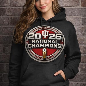 Può includere: Felpa con cappuccio nera con una grande grafica circolare. La grafica recita "INDIANA 2026 NATIONAL CHAMPIONS HOOSIERS" in rosso, bianco e oro. Un trofeo è presente al centro. La felpa ha una tasca frontale.