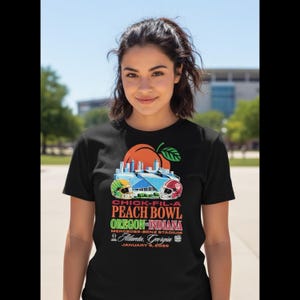 Peut inclure: T-shirt noir avec un graphisme coloré pour le Chick-Fil-A Peach Bowl. Le motif comprend une pêche, un stade et le texte : "OREGON-INDIANA" et "Atlanta, Georgia, January 9, 2020".