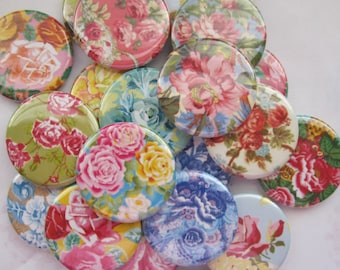 May include: A collection of round floral patterned buttons in various colors, including pink, blue, green, and yellow. The buttons are arranged in a pile, with some overlapping.