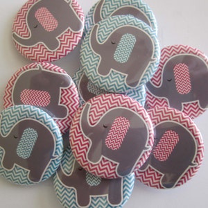 May include: A set of nine round buttons featuring a gray elephant with a pink or blue chevron pattern on a white background. The elephants have a pink or blue chevron pattern on their ears. The buttons are perfect for a baby shower or gender reveal party.