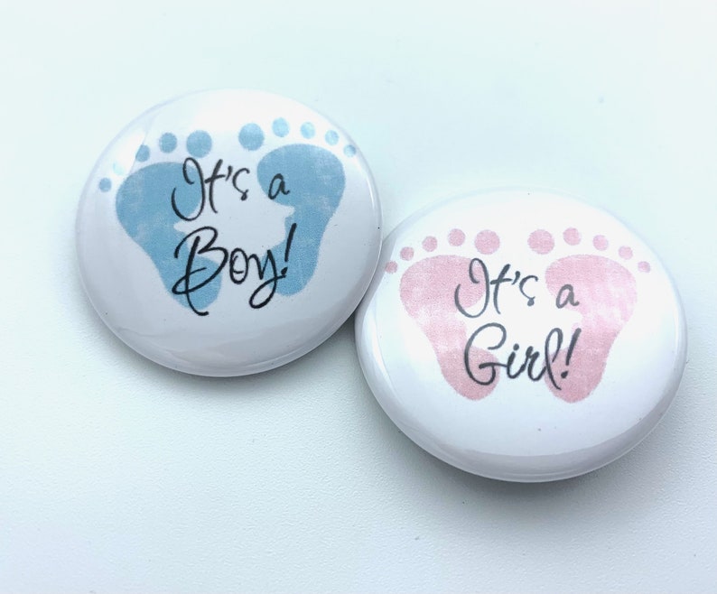 May include: Two round buttons with baby footprints. One button is blue with the text "It's a Boy!" and the other is pink with the text "It's a Girl!"