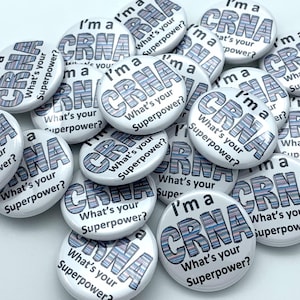 May include: A collection of white round buttons with a blue and pink striped design. The buttons have the text "I'm a CRNA" and "What's your superpower?" printed on them.