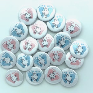 May include: A collection of 18 round baby shower buttons with blue and pink footprints. The buttons have the text "It's a Boy!" or "It's a Girl!" printed on them.
